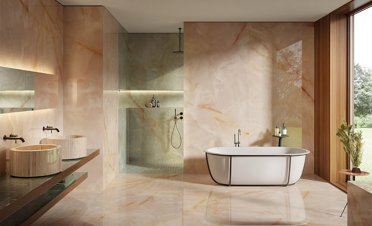 Bathroom with wall and floor tiles in large marble-effect slabs in pink onyx color, double cylindrical striped washbasin in light wood, freestanding bathtub and walk-in shower.